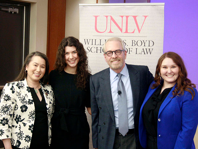 4 people stand in line and smile at camera with a banner in the background that reads UNLV Williams S. Boyd School of Law.