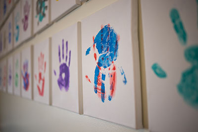 Painted hands in multiple colors on rows of canvas, hanging on a wall.